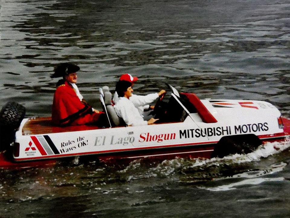 Model konsep amfibia yang menggunakan nama "El Lago Shogun" bagi pasaran UK sedang belayar di atas air, membawa pemandu dan penumpang yang memakai pakaian rasmi istiadat berwarna merah.