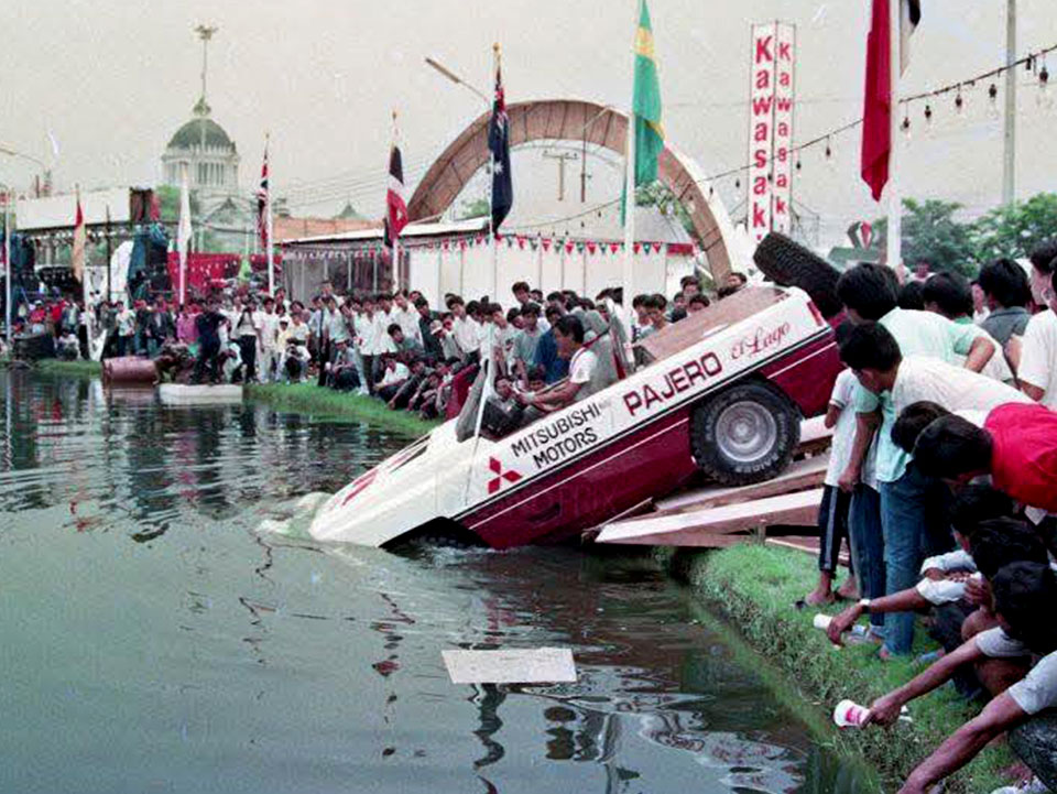 Gambar sejarah memaparkan Mitsubishi Pajero El Lago dipandu turun dari tanjakan kayu khas dan 'terjun' masuk ke dalam tasik sambil disaksikan oleh orang ramai di Bangkok International Motor Show 1988.
